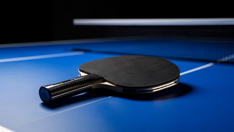 Raquette de ping-pong luxueuse en fibre de carbone posée sur une table bleue, éclairée comme un produit haut de gamme.
